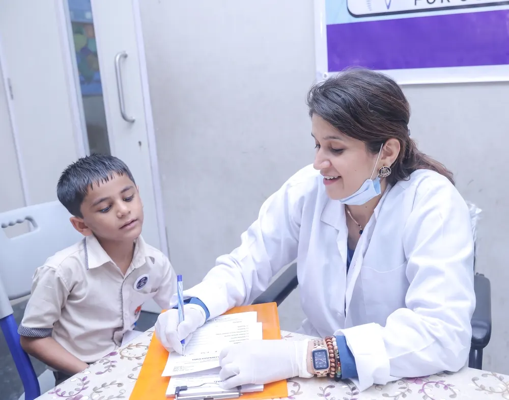 Dr. Vinaya Kamath making notes while talking with a young school-going patient